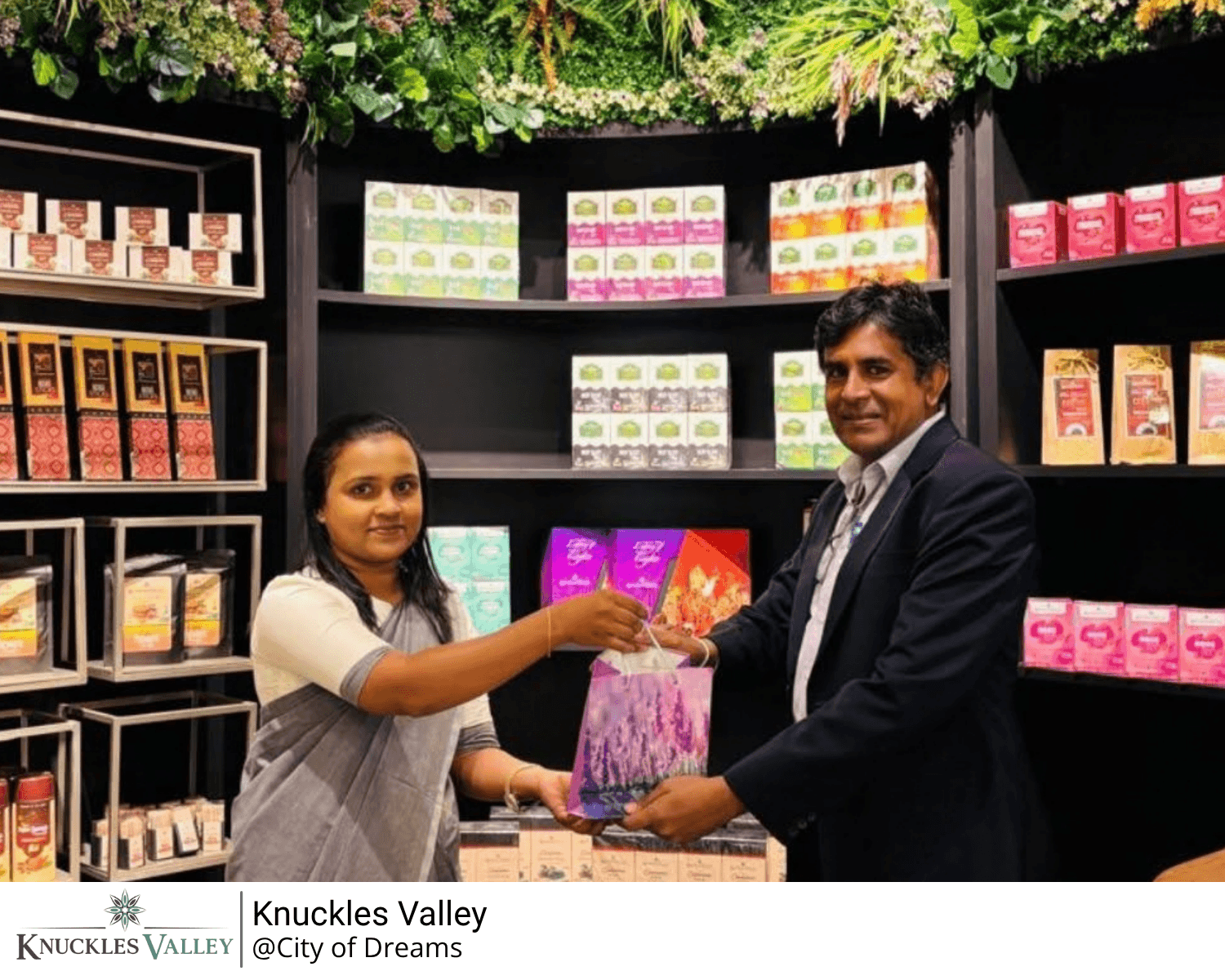 A woman and a man hold a gift together inside the Knuckles Valley store, with branded shelves behind them.