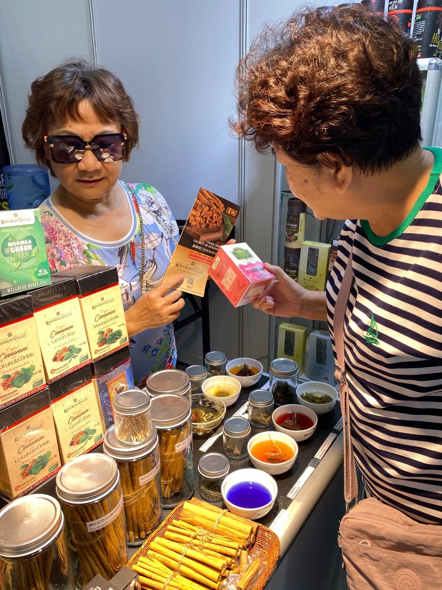Two women talk beside tasting bowls and cinnamon jars at the Knuckles Valley stand.