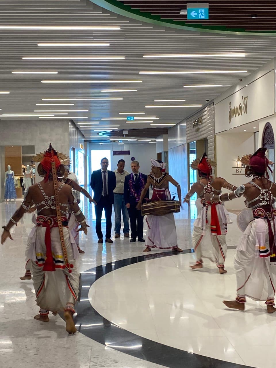 Traditional dancers welcome a group of guests along an indoor walkway.