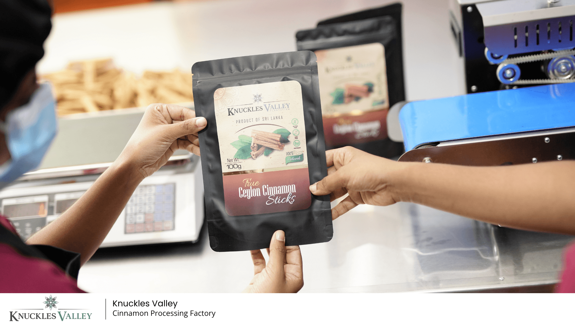 Team members inspect a Knuckles Valley cinnamon package beside packing equipment.