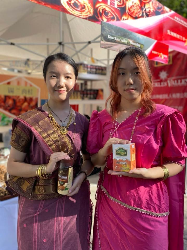 Two women pose with Knuckles Valley products in front of an exhibition display.