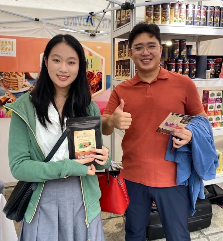Two visitors hold packaged cinnamon products beside the Knuckles Valley display.